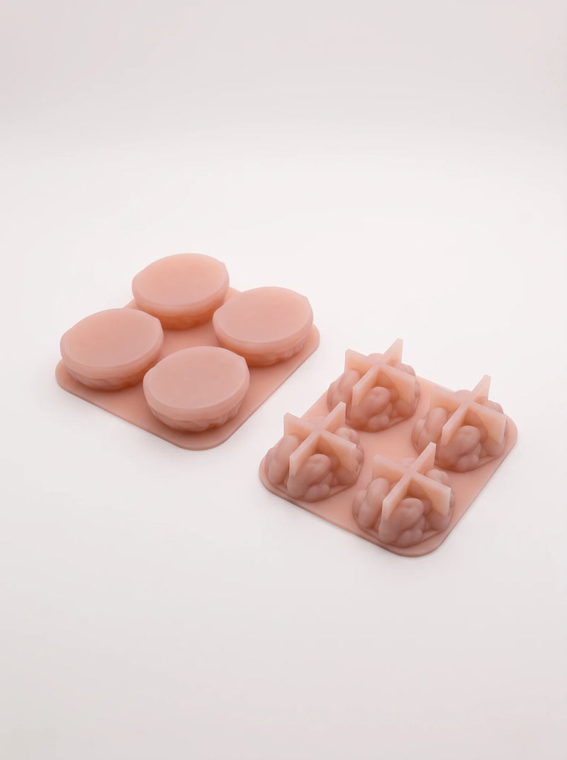Underside view of pink walnut molds, showing rounded shell backs and cross-shaped supports beneath the kernel forms.