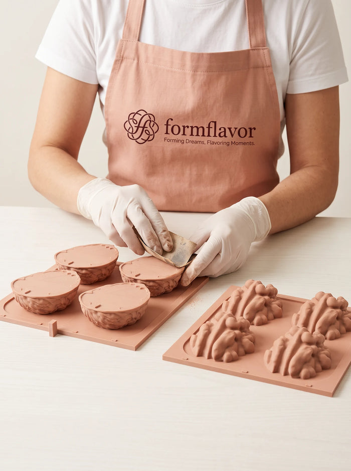 Gloved hands sand a peach-colored walnut shell master model on a tray, with raised kernel master models on a second tray.