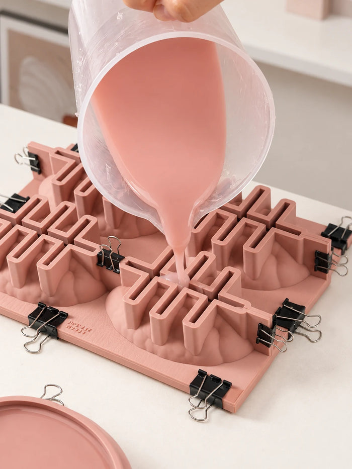 Pink liquid streams from a clear jug into a frame around pecan kernel master models, with black binder clips holding the assembly together.