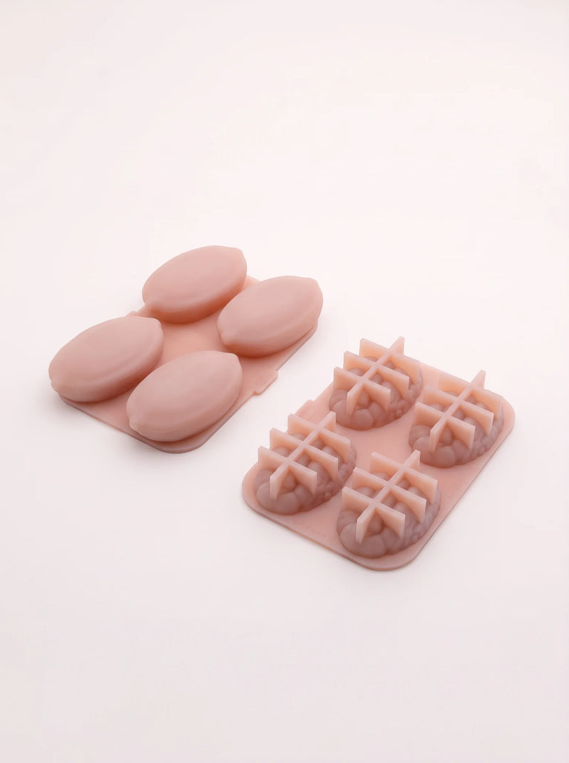Undersides of two pink pecan molds, showing smooth oval shell forms on the left and textured kernel forms crossed by raised ribs on the right.