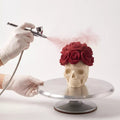 Applying a velvet spray finish to the Eternal Bloom rose skull mousse cake