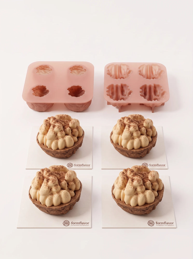 Four walnut-shaped cakes with ivory kernel tops and brown textured shell bases, arranged on square cards in front of pink molds.