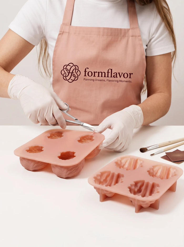 Gloved hands hold scissors at the edge of a pink walnut shell mold; a kernel mold rests nearby.